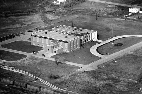 Black and white aerial photo of the Robertson Lignite Research Laboratory in 1950. The front car park is off center with the building.