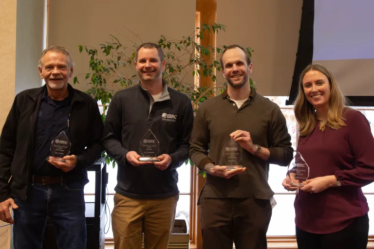 Four EERC employees stand side by side for a photo each holding a glass award